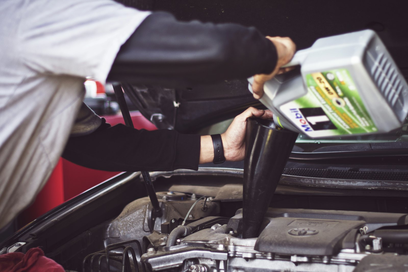 A mechanic pouring oil under a bonnet — working at the coal face